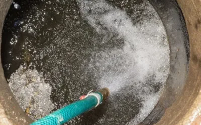 Hose spraying water into a septic tank, illustrating sludge management and wastewater treatment for municipal systems.