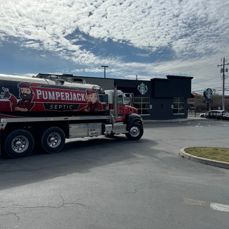 PumperJack Septic performing commercial drain cleaning service in a restaurant parking lot using a vacuum hose and safety barriers in the Finger Lakes