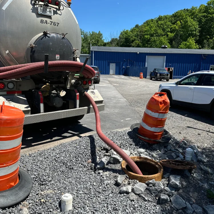 Septic pumping truck connected to a manhole, with safety cones and gravel surrounding the site, illustrating PumperJack's commercial septic services.
