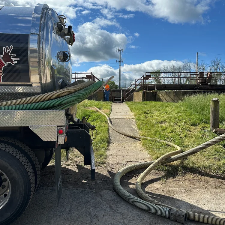 Industrial Sewer Clean-Out Industrial sewer clean-out service in action, featuring a vacuum truck with hoses extending towards a lift station, ensuring efficient wastewater management and compliance.