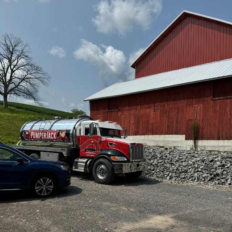 Industrial Wastewater Solutions PumperJack septic service truck parked near a red barn, showcasing industrial wastewater management solutions in a rural setting.