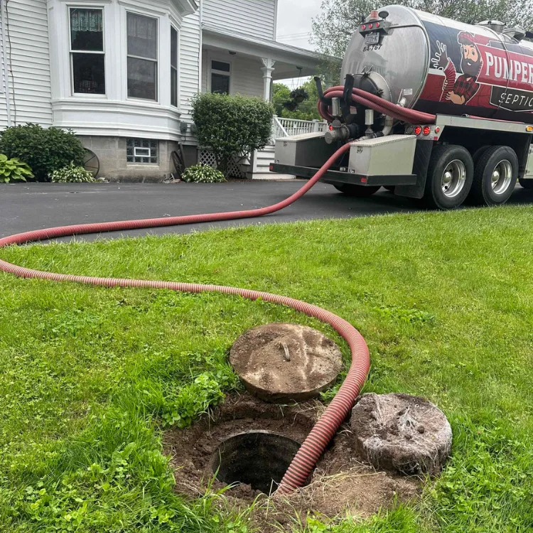 Residential Septic Pumping Residential septic pumping service by PumperJack Septic, vacuum truck connected to septic tank, grassy yard, home in background.