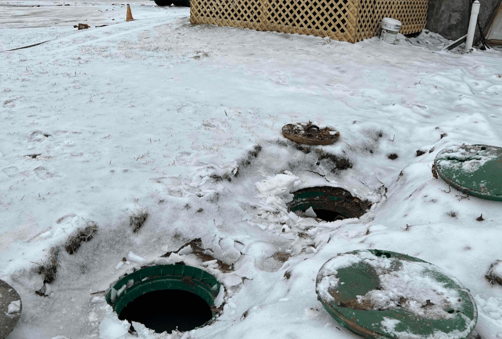 Snow-covered yard with open septic tank access lids showing winter septic service and cold-weather maintenance conditions
