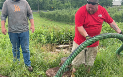 Two technicians performing septic system maintenance, one operating a vacuum hose and the other observing, surrounded by green grass and a rural setting, related to septic services in the Finger Lakes region.